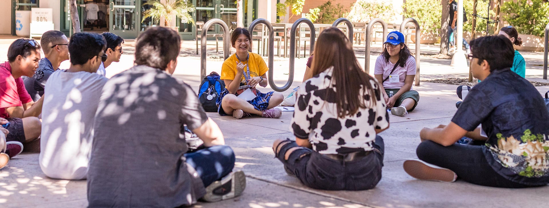 A group of incoming students relax outside the UCR campus bookstore with their leader at Highlander Orientation.
